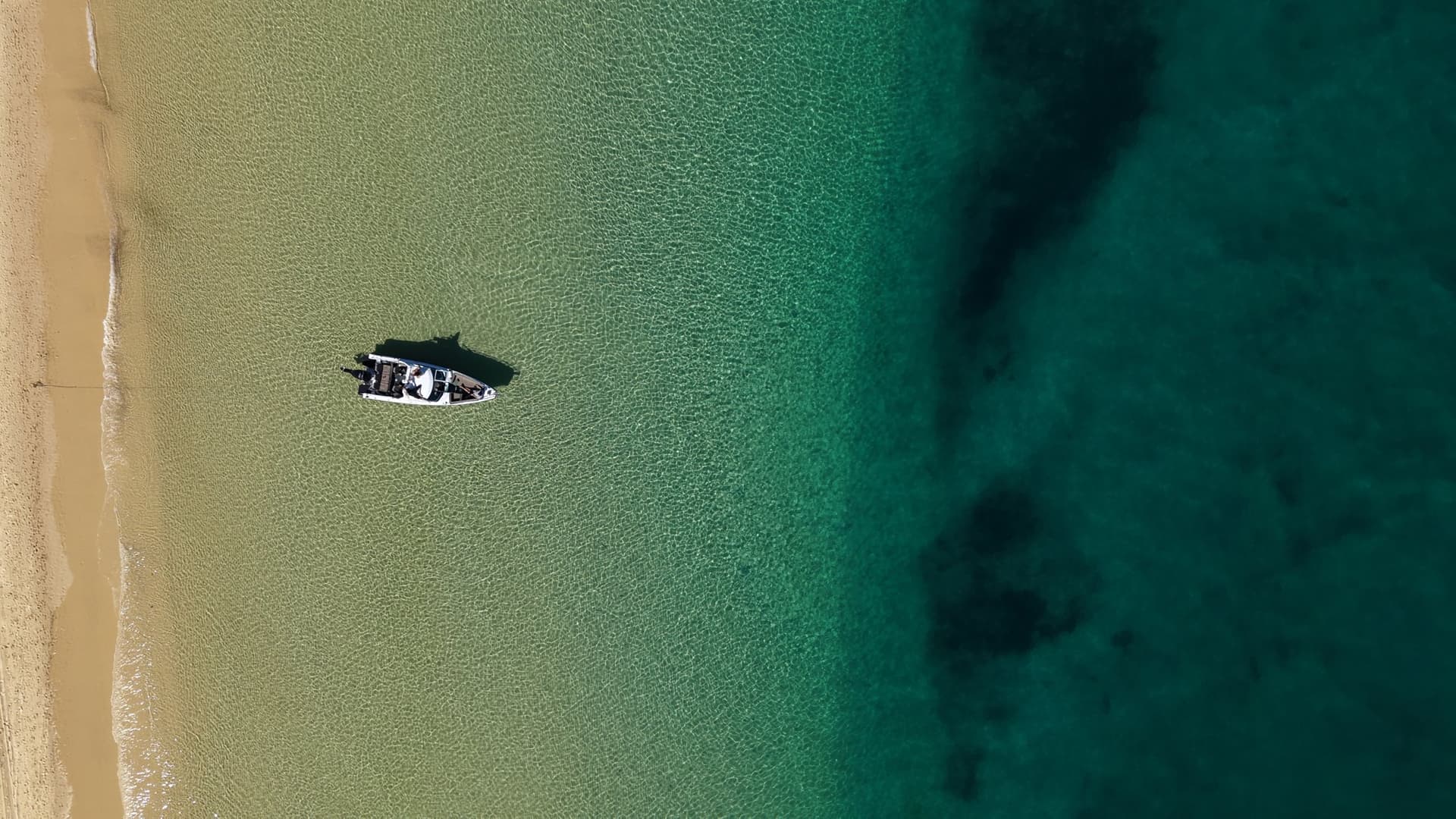 Straight down aerial of the Sea La Vie boat alone on clear shallows beside an empty sandbank