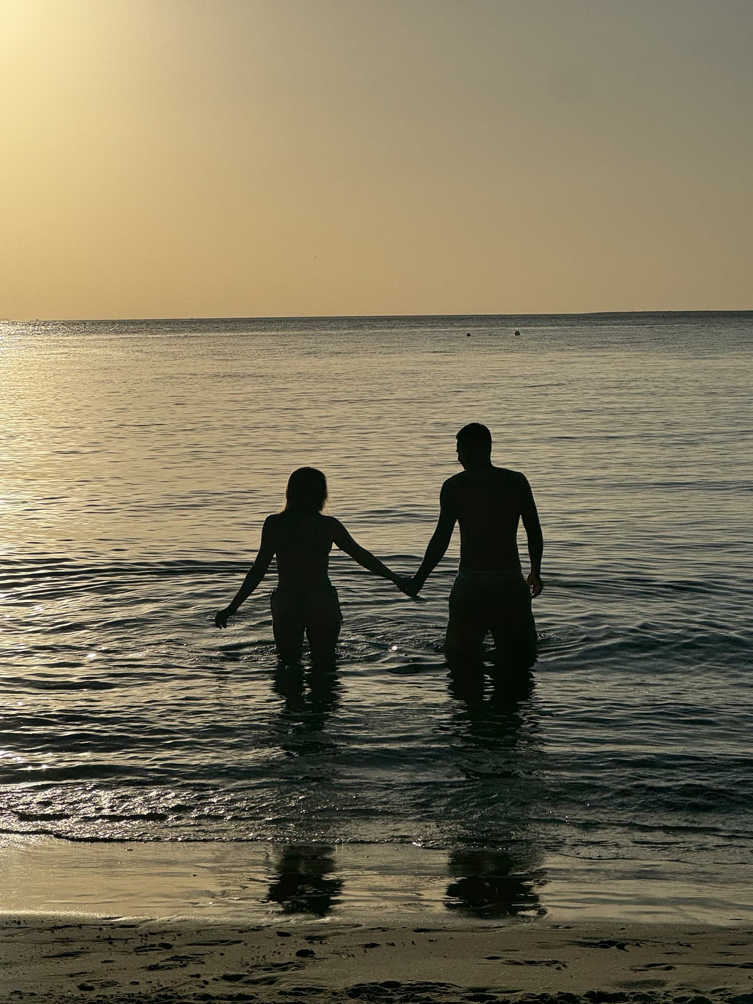 A couple silhouetted hand in hand walking into a golden sunset on the water