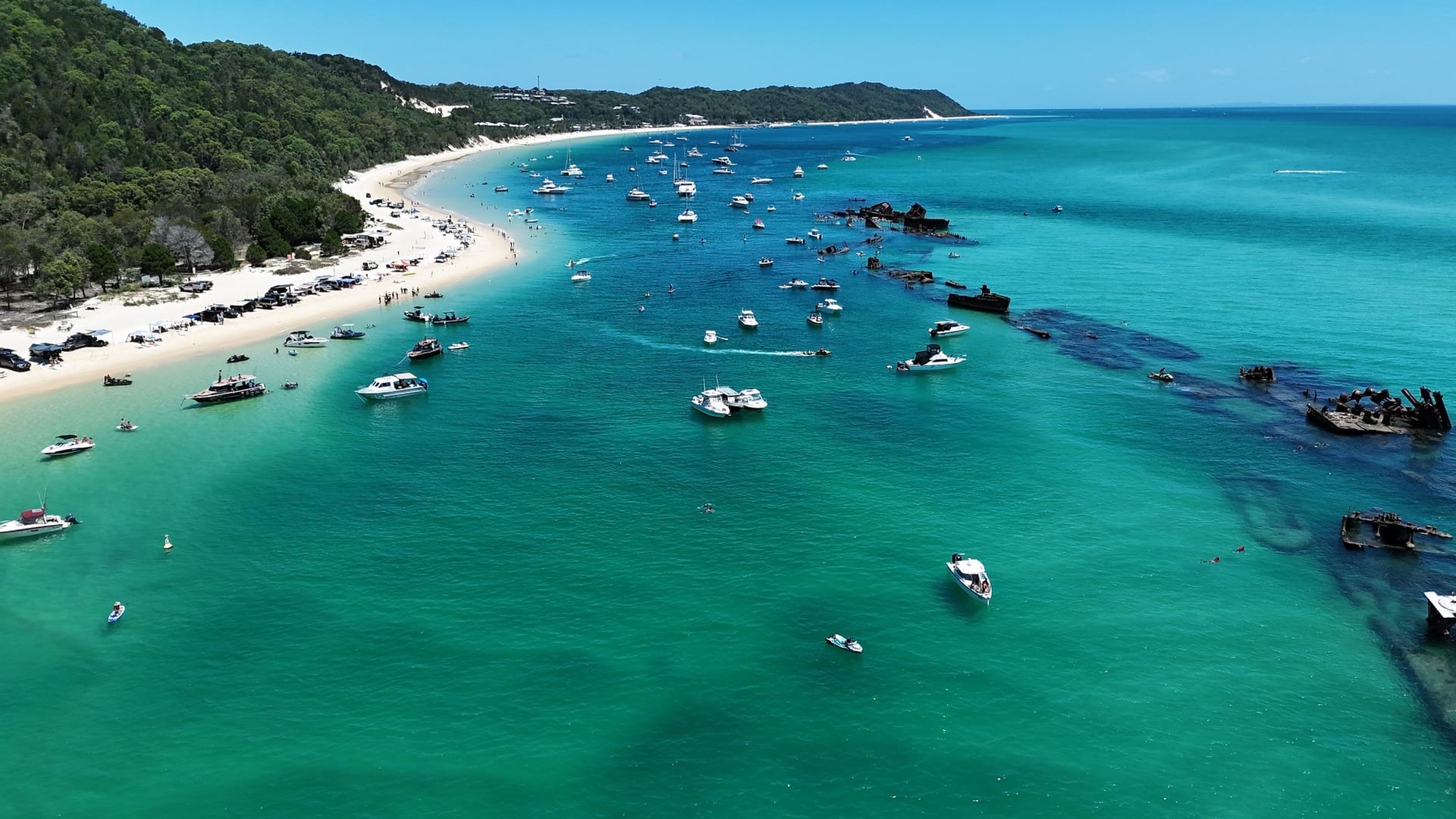 Drone view along the curve of Tangalooma beach with the wreck line dividing two shades of turquoise