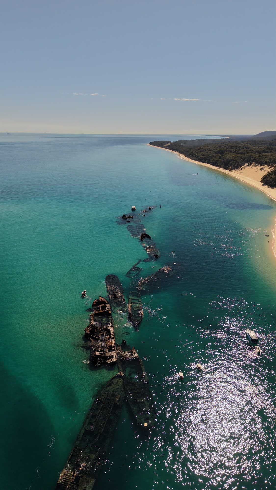 Aerial of the Tangalooma wreck line in turquoise water with snorkellers drifting below